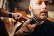 Fotográfia Male barber cutting beard of client in barber shop, South_agency